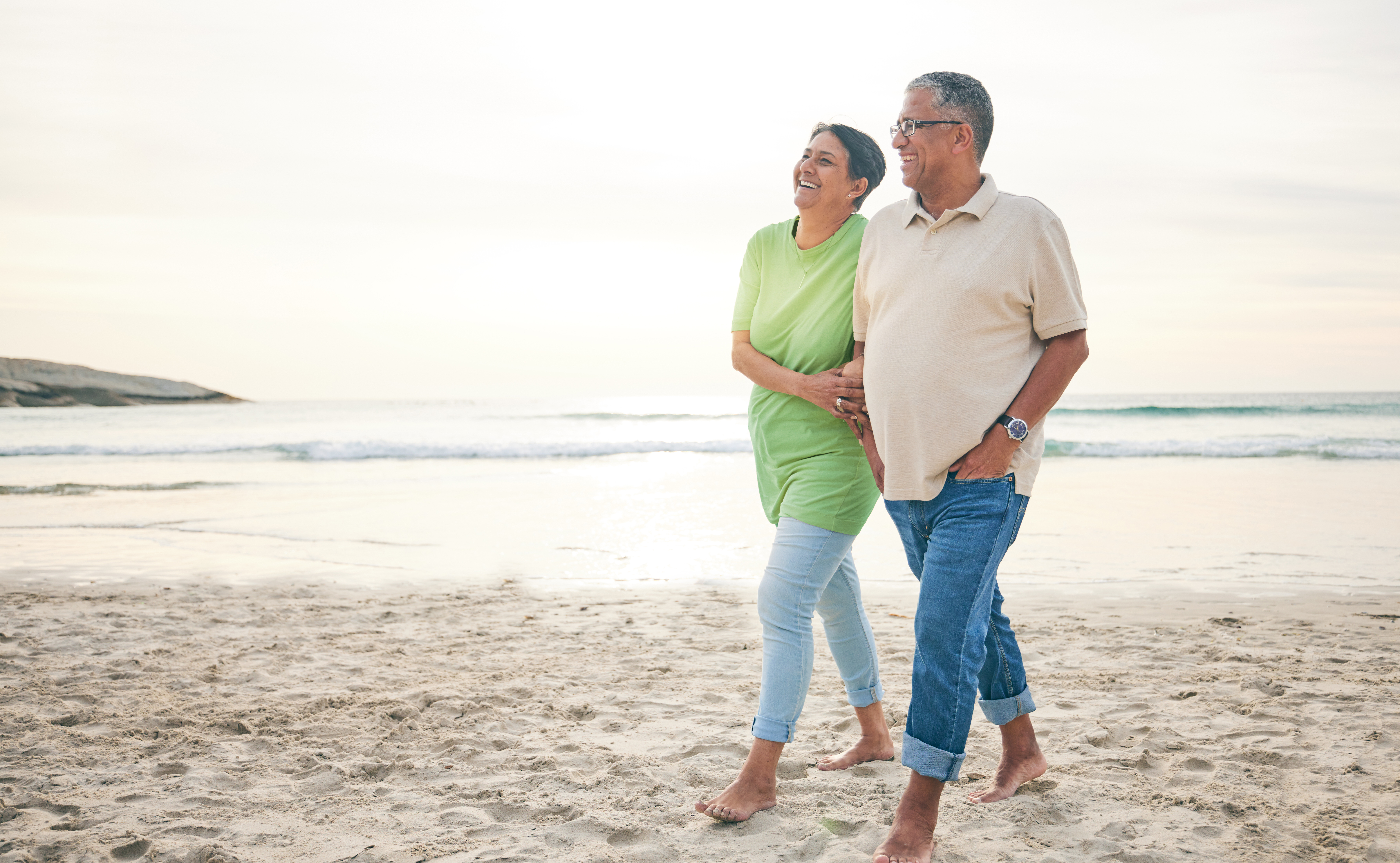 Senior couple walking barefoot on the beach.